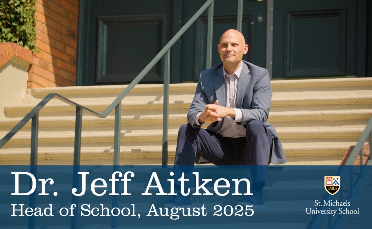 A photo of Dr. Jeff Aitken sitting on the steps of the School House Building looking out towards the field. 