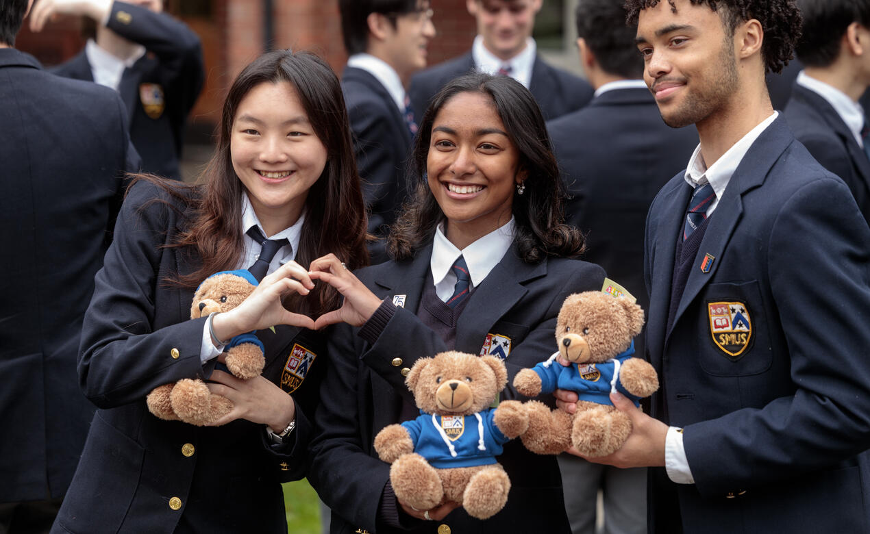Three Senior School students pose holding their grad teddy bear with two of the female students making a heart together with their hands.