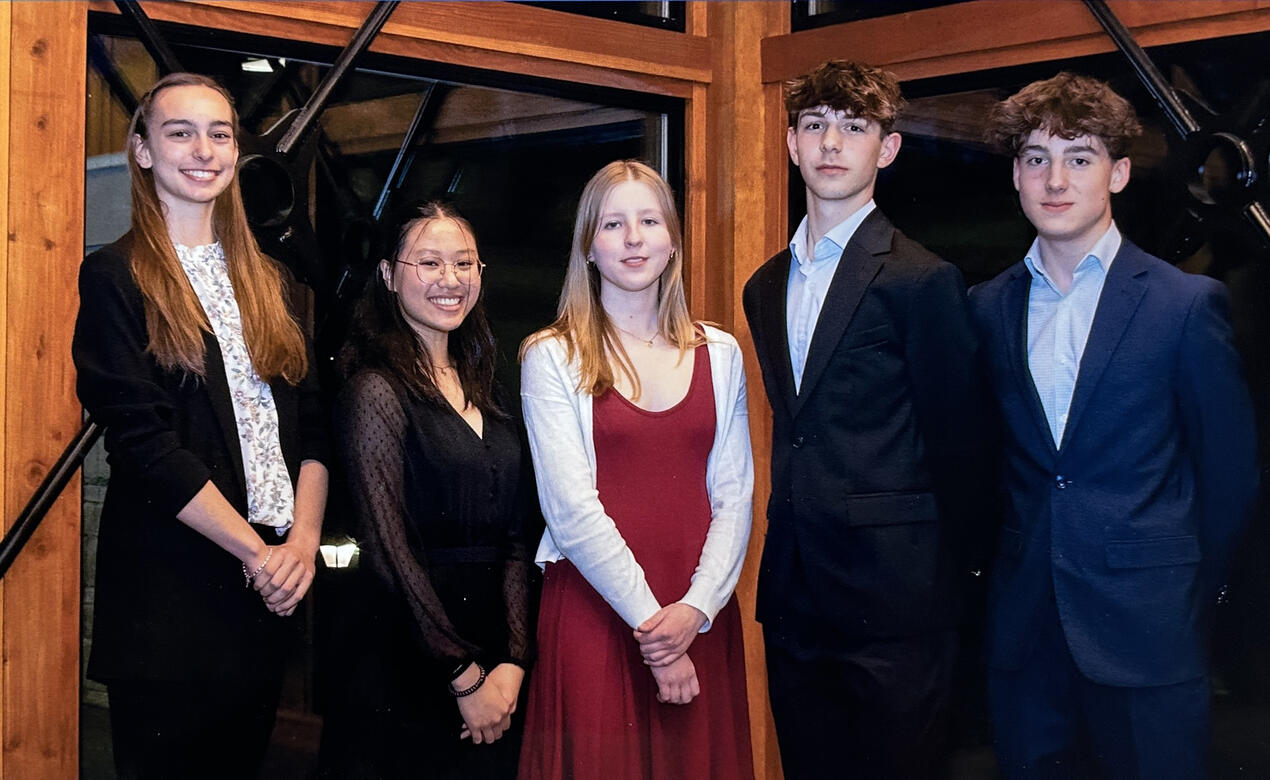 Five students in formal wear pose for a photo at an evening event.