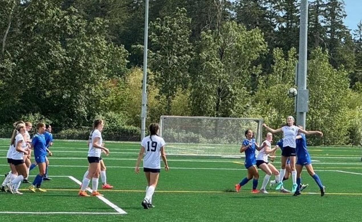 An action shot from a senior girls soccer game where one player is going up for a header as other watch on.