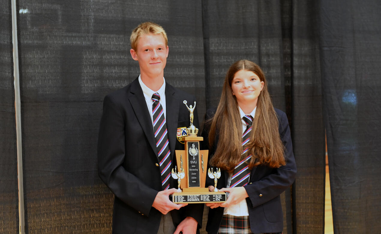 Indigo Edgington and Quinn McMeekin stand beside each other each with a hand on a trophy for Junior Athlete of the Year.