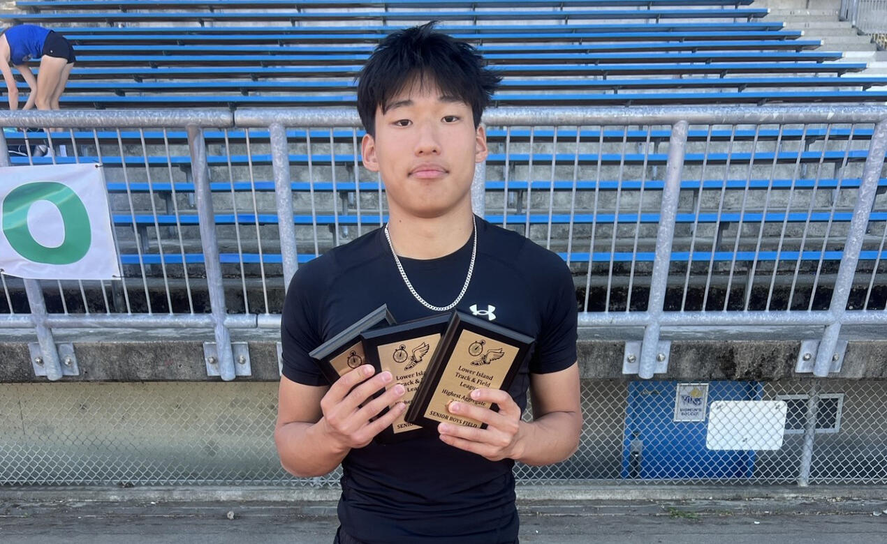 Grade 12 student Leupold Wang stands in front of the stadium stands holding three awards. 