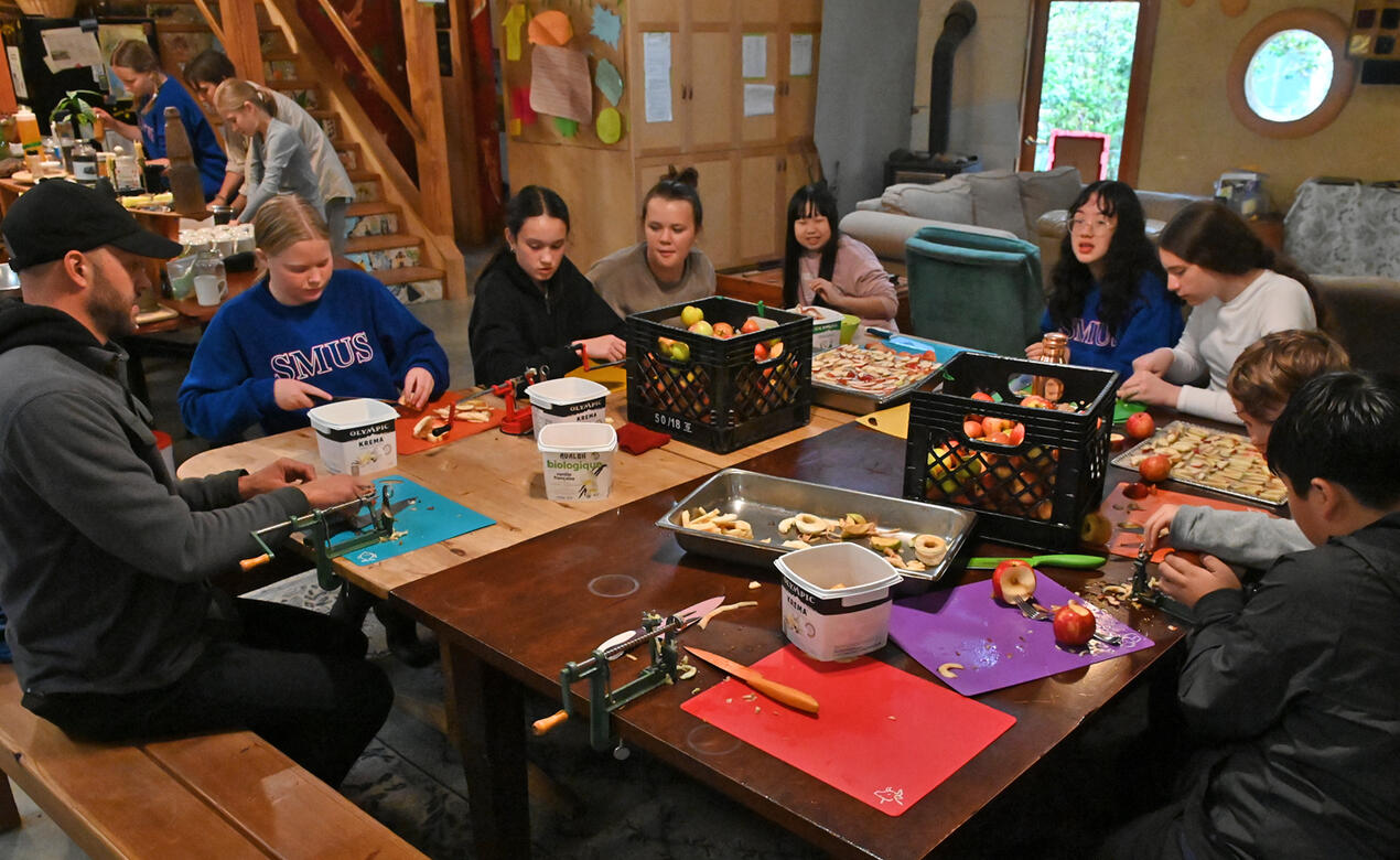 Students sit at a large table peeling and cutting apples