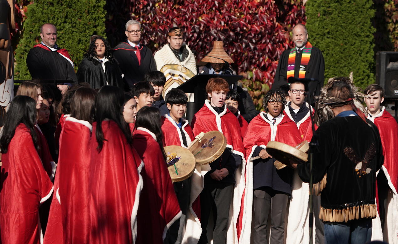 Senior Choir wearing red blankets perform in song and with drums as Elder Willie Pierre guides them 