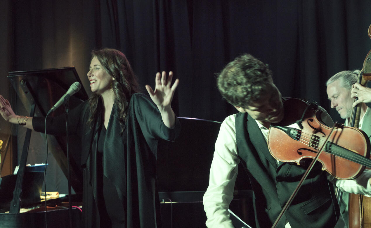 Cari Burdett singing into a microphone with a orchestra accompanying her