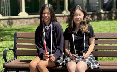 Addy Newman-Ting and Anysia Tam sit on a bench at SMUS posing with their jump ropes resting aroundtheir necks