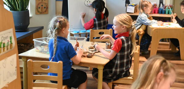 Two young students sit at a table together interacting and playing.