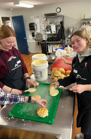 Two Grade 10 students butter bread to contribute to the Rainbow Kitchen Society pantry