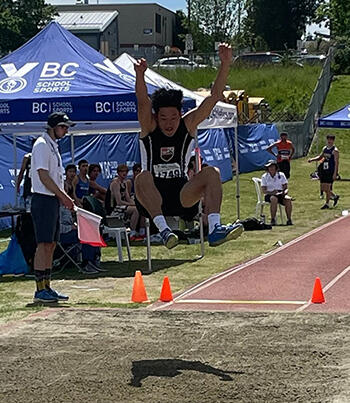 Track and Field's Leupold Wang is in mid-air as he competes in long jump at the Provincial Championship.